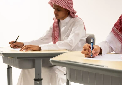 المثابرة والجد للحصول على التفوق العلمي، العودة إلى المدارس، بورترية لطالبان عربيان خليجيان سعوديان يرتدين الثوب الابيض و الشماغ يجلسان على الطاوله فى الفصل يقومان بحل الواجبات ومراجعة الدروس، خلفية بيضاء