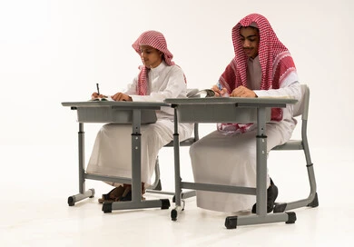 Diligence in studying for a bright future, back to school, a portrait of two Arab Gulf students from Saudi Arabia wearing white thobes and shemaghs sitting at a table in the classroom solving homework and reviewing lessons, white background.