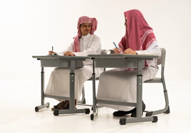 Diligence and commitment to achieving success goals, back to school, a portrait of two Arab Gulf students from Saudi Arabia wearing white thobes and shemaghs sitting at a table in the classroom solving homework and reviewing lessons looking at each other, white background.