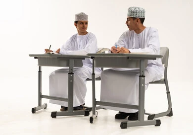 العودة إلى المدارس، الجد والاجتهاد للوصول إلى النجاح والتفوق، بورترية لطالبان عربيان خليجيان عمانيان يرتديان الدشداشة و الكمة يجلسان على الطاوله فى الفصل يقومان بحل الواجبات ومراجعة الدروس ينظران الى بعض، خلفية بيضاء