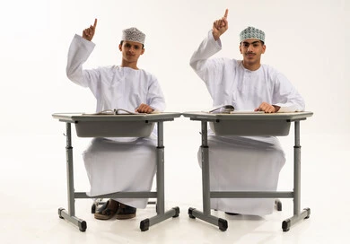 التربية والتعليم بالمناهج المقررة للطلاب في سلطنه عمان، المشاركة والتفاعل داخل الفصل الدراسي، بورترية لطالبان عربيان خليجيان عمانيان يرتديان الدشداشة و الكمة يجلسان على الطاوله يقومان برفع ايديهم للإجابة ، تعابير وايماءات الحماس لمعرفة الجواب الصحيح، خلفية بيضاء