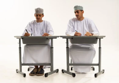 The educational system in the Sultanate of Oman, a portrait of two Omani Gulf Arab students wearing the dishdasha and kumma sitting at a table, doing their homework, preparing for the new school year, back to school, white background.