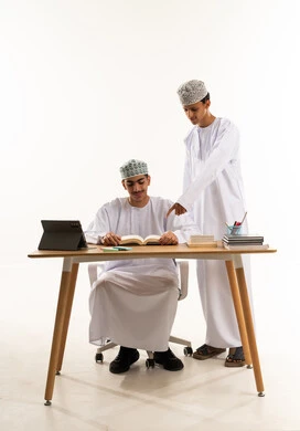 Referring to something, doing homework, a portrait of two Arab Gulf Omani students wearing the dishdasha and kumma sharing information, discussing study materials, a new classroom, education in the Sultanate of Oman, white background.