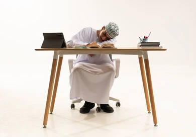 التعب والاجهاد اثناء مراجعة الدروس اليومية، المذاكرة لأوقات متاخرة من الليل، السعي للتفوق والنجاح، بورتريه لطالب عربى خليجي عماني يرتدي الدشداشة و الكمه نائم على طاولة الدراسة، دخول وقت النوم، خلفية بيضاء