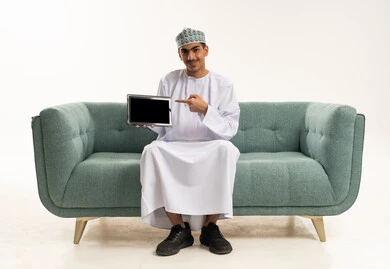 A blank black screen displayed on the tablet, browsing social media, using modern technology and techniques, a portrait of a young Arab Gulf Omani man wearing a dishdasha and kumma sitting on the sofa holding the tablet and pointing at it, looking at the camera with gestures of happiness and joy, white background. A blank black screen displayed on the tablet, browsing social media, using modern technology and techniques, a portrait of a young Arab Gulf Omani man wearing a dishdasha and kumma sitting on the sofa holding the tablet and pointing at it, looking at the camera with gestures of happiness and joy, white background.
