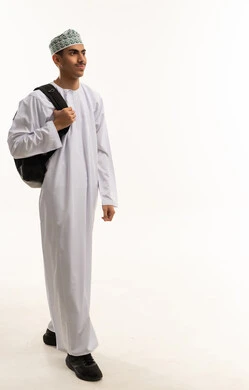 ايماءات المشي و الذهاب إلى مكان معين، مفهوم الاجتهاد للوصول إلى النجاح، المناهج العلمية التعليمية، مفهوم العودة إلى المدارس، بورتريه لطالب عربي خليجي عمانى يرتدي الدشداشة و الكمة يحمل حقيبة الظهرينظر بايماءات السعادة و السرور، صورة لكامل الجسم، خلفية بيضاء