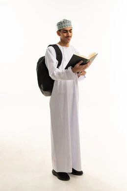 أهمية التعليم في بناء مستقبل مشرق للمجتمع، بورتريه لطالب عربي خليجي عمانى يرتدي الدشداشة و الكمة يحمل حقيبة الظهر يقوم بقراءه الكتب ، التعليم في سلطنه عمان،ايماءات الاندماج و التركيز، الجسم بالطول الكامل، خلفية بيضاء