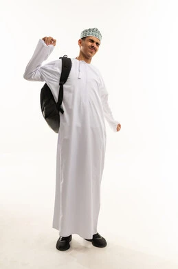 مفهوم النشاط والإستيقاظ الصباحي، بورتريه لطالب عربي خليجي عماني يرتدي الدشداشة و الكمه و الحقيبه المدرسيه يرفع يديه بإيماءات تدل على التمدد ، الإستعداد للعام الدراسي الجديد، التعليم الدراسي في سلطنه عمان، الجسم بالطول الكامل، خلفية بيضاء