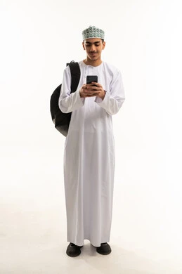Gestures of integration and focus, chatting with friends online, a portrait of an Arab Gulf Omani student wearing a dishdasha and kumma carrying a bag on his back, following social media news using a mobile phone, browsing mobile applications, full-body image, white background.