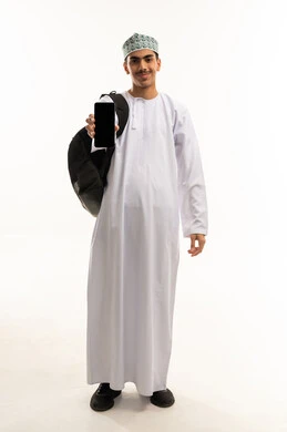 The use of modern technical devices, looking at the camera with gestures of happiness and joy, a portrait of an Arab Gulf Omani university student wearing a dishdasha and kumma, carrying a bag on his back and holding a mobile phone in his hands, displaying a blank black screen on the phone, full-body shot, white background.