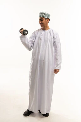 رفع الأوزان الحديدية الثقيلة، نشاط بدني للمحافظة على الصحة واللياقة الجسدية، بورترية لشاب عربي خليجي عماني يرتدي الدشداشة و الكمه  يمارس التمارين الرياضية مع الدمبل، كمال الأجسام و بناء العضلات ، تمارين رفع الأثقال(دمبلز)، ايماءات بذل الجهد والتعب، الجسم بالطول الكامل، خلفية بيضاء
