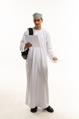 الاستعداد للعام الدراسي الجديد، التعليم  الثانوي في سلطنه عمان, بورتريه لطالب ثانوي عربي خليجي عماني يرتدي الدشداشة و الكمة يحمل حقيبة على ظهره ويمسك بيديه ورق دراسي , الجسم بالطول الكامل, خلفية بيضاء