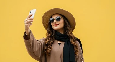 استخدام الهاتف المحمول بايماءات السعادة والفرح، الاهتمام بالاناقة والمظهر الخارجي، بورتريه مقرب لصبية عربية خليجية سعودية ترتدي الزي الكاجوال وقبعة القش تضع النظارات الشمسية تقوم بالتقاط صور سيلفي شخصية، خلفية صفراء