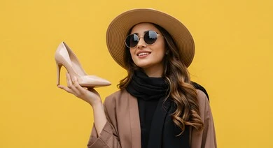 مواكبة تصاميم الأزياء والموديلات الحديثة, بورتريه مقرب لصبية عربية خليجية سعودية ترتدي الزي الكاجوال وقبعة الق تضع النظارات الشمسية تحمل بيدها كعب نسائي بايماءات الأنوثة واللطافة, التسويق للمنتجات السعودية والماركات العالمية الفاخرة، خلفية صفراء