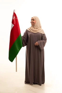 Commemoration of the establishment of the state in 1775 AD, cultures and national symbols, love for the homeland and belonging to it, a portrait of an elderly Arab Omani Gulf woman wearing a hijab and an abaya holding the national flag of the country celebrating the anniversary of Omani National Day on November 18, full-body, white background.