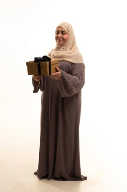 الاحتفال بأعياد الميلاد, التعبير عن المحبة والتقدير, تقديم الهدايا في المناسبات السعيدة, بورترية لإمراة كبيرة بالسن عربية سعودية خليجية محجبة ترتدي العباءة تمسك بيديها علبة هداية, الجسم بالطول الكامل، خلفية بيضاء