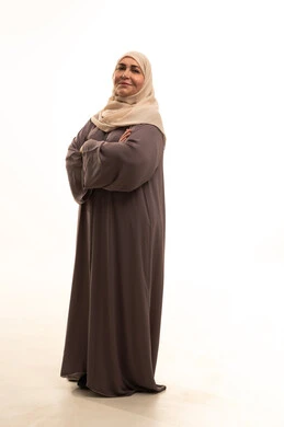 Looking at the camera with gestures of joy and self-confidence, the concept of elegance and attention to appearance, a portrait of an elderly Arab Saudi Gulf woman wearing a hijab and an abaya, standing with arms crossed, full-body image, white background.