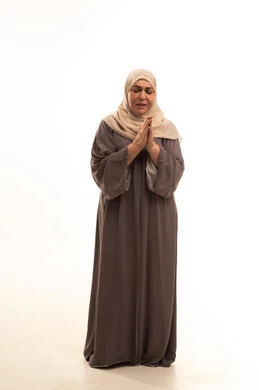 Snowfall season, enjoying the cold snowy winter atmosphere, feeling the frost, shivers, and freezing, a portrait of an elderly Arab Saudi Gulf woman wearing a hijab and an abaya feeling very cold, full-body, white background.