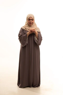 Enjoying the cold snowy winter atmosphere, the season of snowfall, feeling the frost, shivering, and freezing, a portrait of an elderly Arab Saudi Gulf woman wearing a hijab and an abaya, feeling very cold, full-body shot, white background.