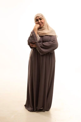 Trying to find a solution to a problem, contemplation, focus, and planning for the future, a portrait of an elderly Arab Saudi Gulf woman wearing a hijab and an abaya, resting her hand on her chin and looking with gestures of thought and reflection, full-body, white background.