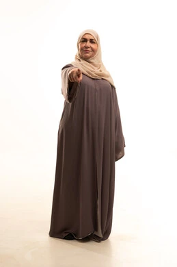Specifying a certain location, hand signals and movements indicating this place (here), a portrait of an elderly Arab Saudi Gulf woman wearing a hijab and an abaya, raising her index fingers and pointing to something, full-body, white background.