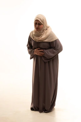 الإحساس بالمغص والوجع، الشعور بحرقة في المعدة، الحاجه للمساعدة وطلب العلاج، بورترية لإمراة كبيرة بالسن عربية سعودية خليجية محجبة ترتدي العباءة تضع يدها على بطنها تنحني من شدة الألم، إيماءات التقيؤ والغثيان، صورة لكامل الجسم، خلفية بيضاء