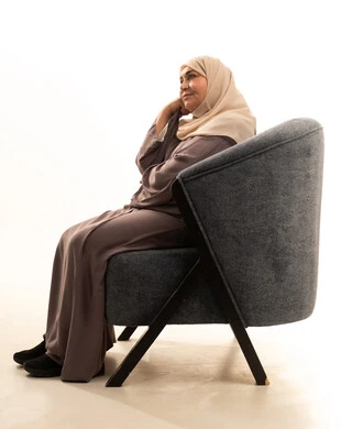 النظر بشرود إلى مكان ما، إيماءات الحيرة والقلق, التمعن والتركيز والتخطيط للمستقبل،بورتريه من الجانب لإمراة كبيرة بالسن عربية سعودية خليجية محجبة ترتدي العباءة تجلس على كرسي تضع يدها على ذقنها وتنظر بعيداً بتفكير وتأمل، محاولة إيجاد حل لشيء ما، خلفية بيضاء