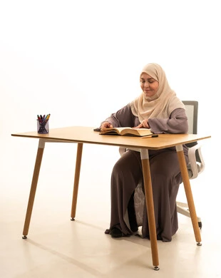 قضاء الوقت بالتعلم والتثقف، ثقافة التعلم الذاتي، الاستمتاع بقراءة الكتب والقصص والروايات،بورتريه لإمراة كبيرة بالسن عربية سعودية خليجية محجبة ترتدي العباءة تجلس على الطاولة امامها كتاب، خلفية بيضاء