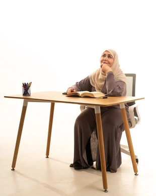 قضاء الوقت بالقراءة والتعلم والثقافة، وفهوم التثقيف الذاتي، بورتريه لإمراة كبيرة بالسن عربية سعودية خليجية محجبة ترتدي العباءة تجلس على الطاولة امامها كتاب تثقيفي، ايماءات التفكير فى شيء ما ، خلفية بيضاء