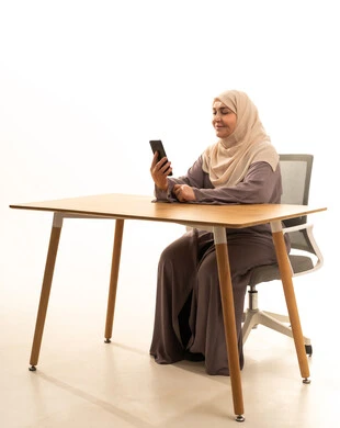 التسويق الالكترونى، استخدام جهاز تقني حديث ومتطور، تصفح مواقع التواصل الاجتماعي، الدردشة مع الأصدقاء والأقارب عبر الجوال، بورتريه لإمراة كبيرة بالسن عربية سعودية خليجية محجبة ترتدي العباءة تجلس على الطاولة تمسك بيدها الهاتف المحمول، خلفية بيضاء