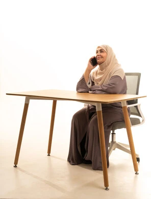 التواصل مع العائلة والأصدقاء, استخدام الأجهزة التقنية الحديثة في الحياة اليومية, مشاركة الأخبار والأحاديث الجيدة, بورتريه لإمراة كبيرة بالسن عربية سعودية خليجية محجبة ترتدي العباءة تجلس على الطاولة تمسك بيدها الهاتف المحمول, شابة سعودية تقوم بإجراء اتصال هاتفي, خلفية بيضاء