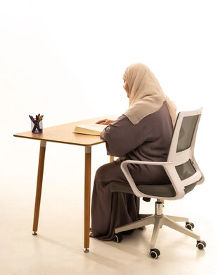 القراءة بتمعن وتركيز، قضاء وقت الفراغ بالتعلم والثقافة، بورتريه من الجانب لإمراة كبيرة بالسن عربية سعودية خليجية محجبة ترتدي العباءة تجلس على الطاولة امامها كتاب تثقيفي ، خلفية بيضاء