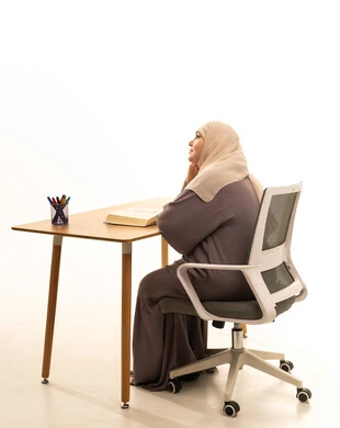 قضاء وقت الفراغ بالتعلم والثقافة، بورتريه من الجانب لإمراة كبيرة بالسن عربية سعودية خليجية محجبة ترتدي العباءة تجلس على الطاولة امامها كتاب تثقيفي، ايماءات التفكير فى شيء ما ، خلفية بيضاء