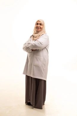Providing medical assistance to patients, working in medical centers and hospitals, a portrait of an elderly Arab Gulf Saudi female doctor wearing a medical coat standing with crossed arms, the concept of medicine and healthcare, a young Saudi woman looking at the camera with gestures of joy, full-body image, white background.