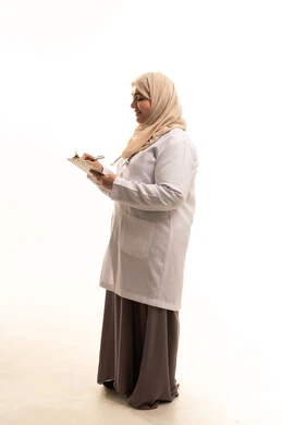 Listening to the patient's condition with an open heart and a smile, providing medical consultations and health services, a side portrait of an elderly Saudi Gulf Arab female doctor wearing a medical coat preparing medical reports, professions and jobs in Saudi Arabia, working in the health sector, full-body, white background.