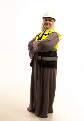 النظر الى الكاميرا بايماءات السعادة و السرور، مفهوم ادارة المشاريع الهندسية، وظائف ومهن نسائية , الوقوف بايماءات الثقة, بورتريه لمهندسة عربية خليجية سعودية كبيرة في السن محجبة ترتدي سترة الحماية والخوذة تقف بايدي متقاطعه، صورة لكامل الجسم، خلفية بيضاء