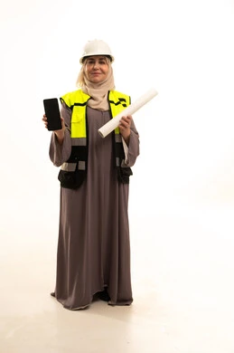 مهن ووظائف نسائية، العمل في القطاع الهندسي، دمج التكنولوجيا الحديثة بالهندسة، بورتريه لمهندسة عربية خليجية سعودية كبيرة في السن ترتدي خوذة وسترة الحماية تمسك بيديها المخطط الهندسي ، عرض شاشة سوداء عبر الهاتف المحمول، صورة لكامل الجسم، خلفية بيضاء