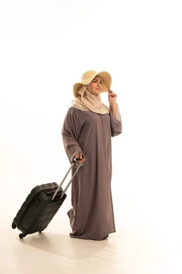 التجهيز للسفر و الرحلات، الذهاب في عطلة صيفية ممتعة  , بورتريه لامرأة عربية خليجية سعودية كبيرة في السن ترتدي العباءة و الحجاب مع قبعة من القش تمسك بيدها حقيبة سفر , النظر بإيماءات الفرح و السرور , صورة للجسم بالطول الكامل , خلفية بيضاء