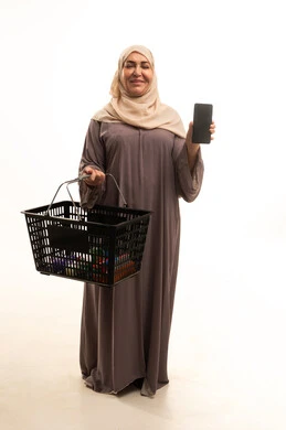 A blank black screen displayed on a mobile phone, looking at the camera with expressions of happiness and joy, shopping at the supermarket, searching for household supplies from the Saudi shopping center, a portrait of an elderly Arab Gulf Saudi woman wearing an abaya holding a shopping basket in her hands, full-body, white background.