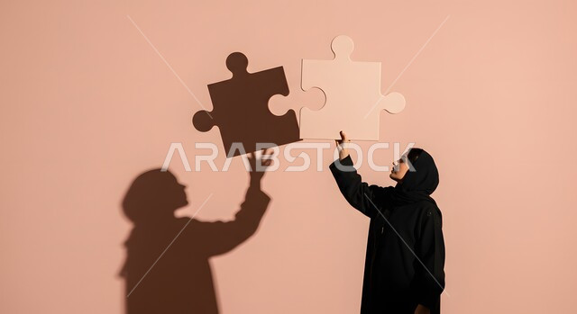 التسلية والترفيه وقضاء وقت ممتع, ألعاب الذكاء وتنمية المهارات, الدقة والتركيز وحل اللغز, بورتريه لسيدة عربية خليجية سعودية محجبة ترتدب عباءة سوداء تحاول ربط وتوصيل قطع البزل, لعبة تركيب الصور، انعكاس الظل على الجدار، خلفية وردية