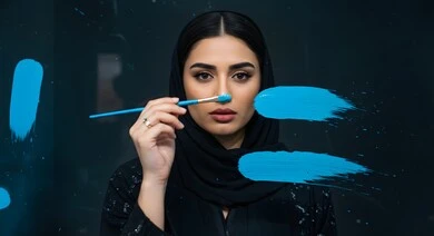 Artistic recreational activities, having fun drawing, close-up of a veiled Saudi Arabian Gulf woman holding a blue paintbrush, practicing the hobby of drawing and coloring, black background