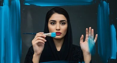 Artistic recreational activities, having fun drawing, close-up of a veiled Saudi Arabian Gulf woman holding a blue paintbrush, practicing the hobby of drawing and coloring, black background
