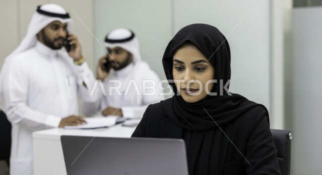 مهنة ووظيفة نسائية مكتبية سعودية، ادارة وانجاز المهام باستخدام جهاز تقني حديث ومتطور, امرأة عربية خليجية سعودية ترتدي الحجاب والعباءة تعمل على الحاسوب المحمول في مقر الشركة، ايماءات وتعابير التركيز والاندماج