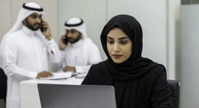 مهنة ووظيفة نسائية مكتبية سعودية، ادارة وانجاز المهام باستخدام جهاز تقني حديث ومتطور, امرأة عربية خليجية سعودية ترتدي الحجاب والعباءة تعمل على الحاسوب المحمول في مقر الشركة، ايماءات وتعابير التركيز والاندماج