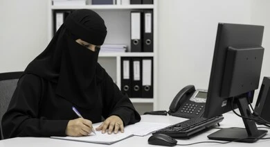 مهنة ووظيفة نسائية مكتبية سعودية، ادارة وانجاز المهام، استخدام جهاز تقني حديث ومتطور, امرأة عربية خليجية سعودية منقبة ترتدي العباءة تقوم بكتابة التقارير في مقر الشركة، ايماءات وتعابير التركيز والاندماج