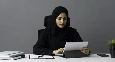 Saudi female office profession and job, managing and completing tasks, using a modern and advanced technical device, a veiled Saudi Arabian Gulf woman wearing an abaya working on a tablet at the company headquarters, gestures and expressions of focus and integration