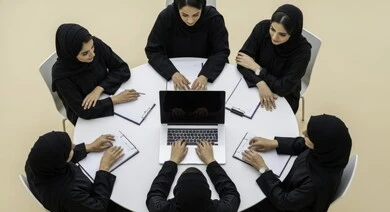 Overhead view of a business meeting between Saudi Arabian Gulf female employees in a conference room. Understanding and cooperation between colleagues to achieve company goals. Comfortable work environment in Saudi companies. Use of modern technical devices in offices. Saudi female office profession and job.