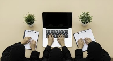 Overhead view of a business meeting between Saudi Arabian Gulf female employees in a conference room. Understanding and cooperation between colleagues to achieve company goals. Comfortable work environment in Saudi companies. Use of modern technical devices in offices. Saudi female office profession and job.