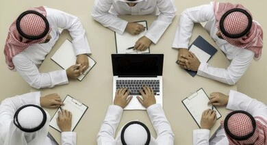 صورة علوية لاجتماع عمل بين موظفين عرب خليجيين سعوديين في غرفة الاجتماعات،  التفاهم والتعاون بين الزملاء لتحقيق أهداف الشركة, بيئة العمل المريحة في الشركات السعودية, استخدام الأجهزة التقنية الحديثة في المكاتب