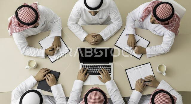 صورة علوية لاجتماع عمل بين موظفين عرب خليجيين سعوديين في غرفة الاجتماعات،  التفاهم والتعاون بين الزملاء لتحقيق أهداف الشركة, بيئة العمل المريحة في الشركات السعودية, استخدام الأجهزة التقنية الحديثة في المكاتب